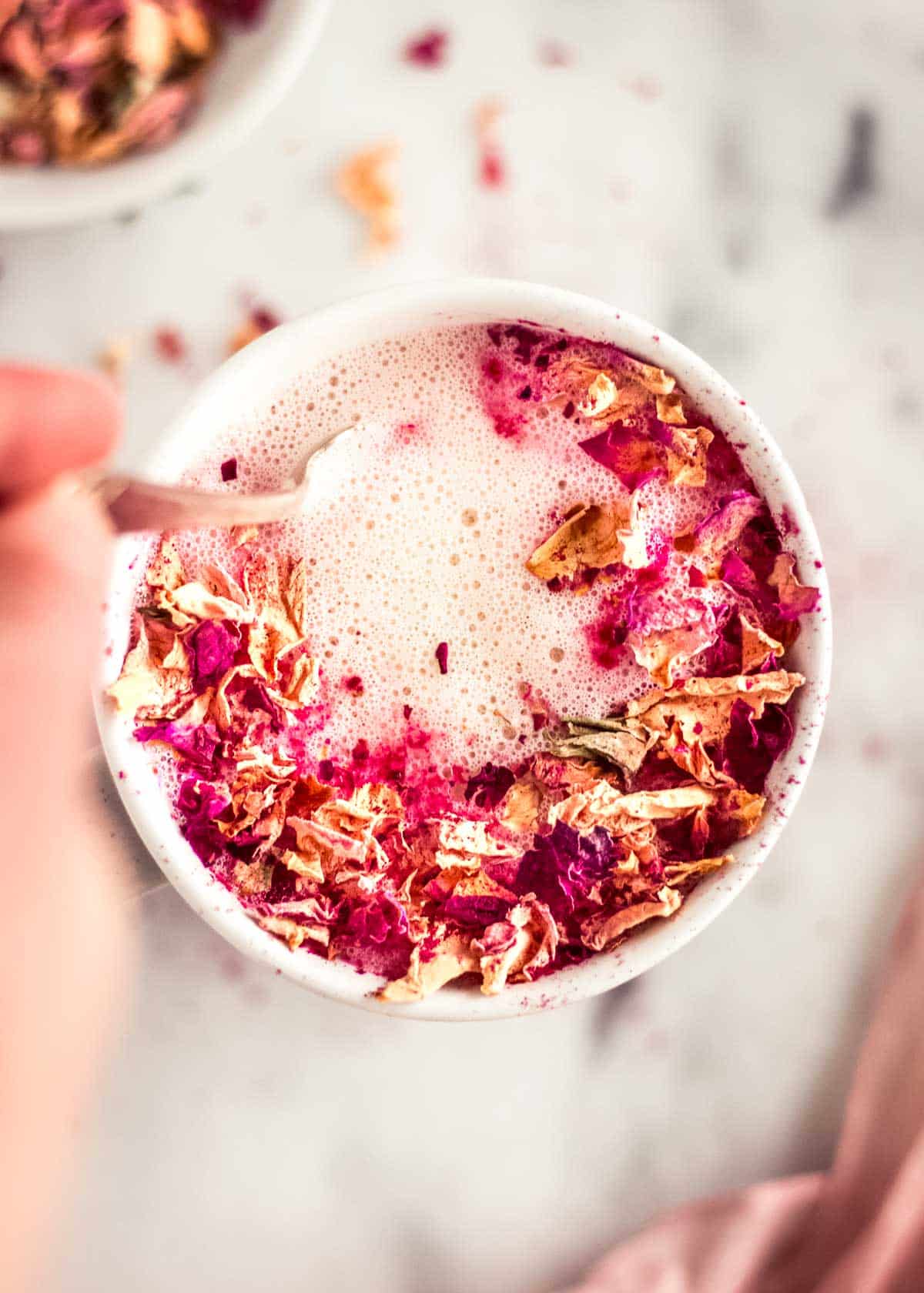 Woman's hand stirring dairy free rose latte decorated with rose petals.
