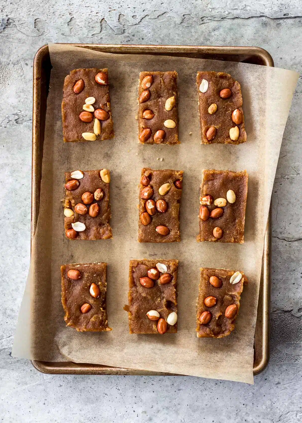 A parchment-lined baking sheet has vegan snickers bars spread over it before they have been covered in chocolate.