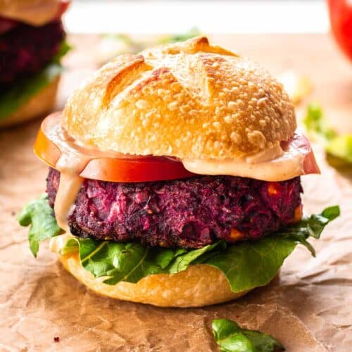 A vegan beet black bean burger sits on brown paper. The burger is served in a sourdough bread bun, with lettuce, tomato and mayo.