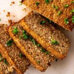 Slices of vegan nut roast on a white chopping board decorated with parsley.