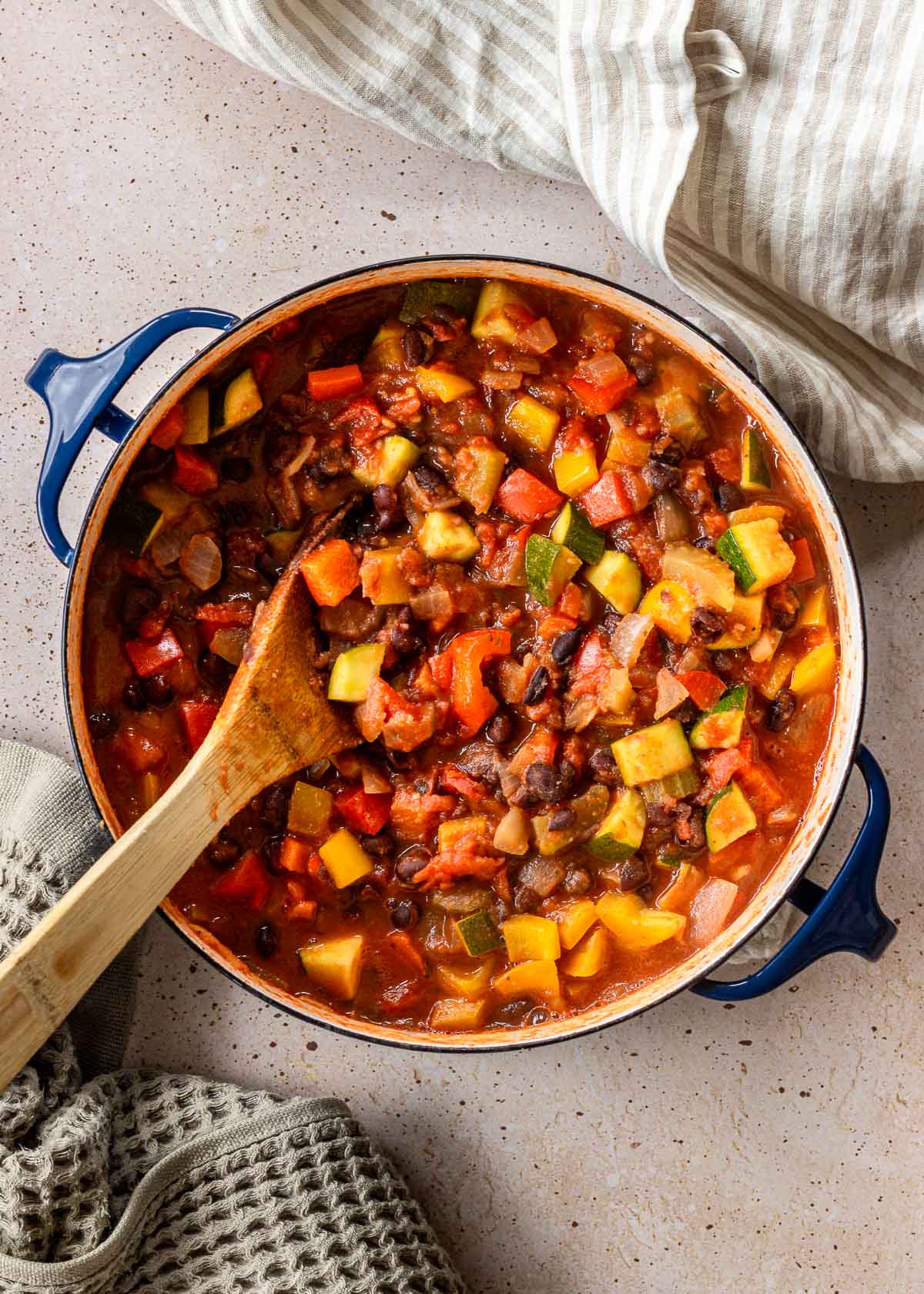 Large blue pot of black bean chili, surrounded by a grey waffle tea towel and a beige striped napkin.